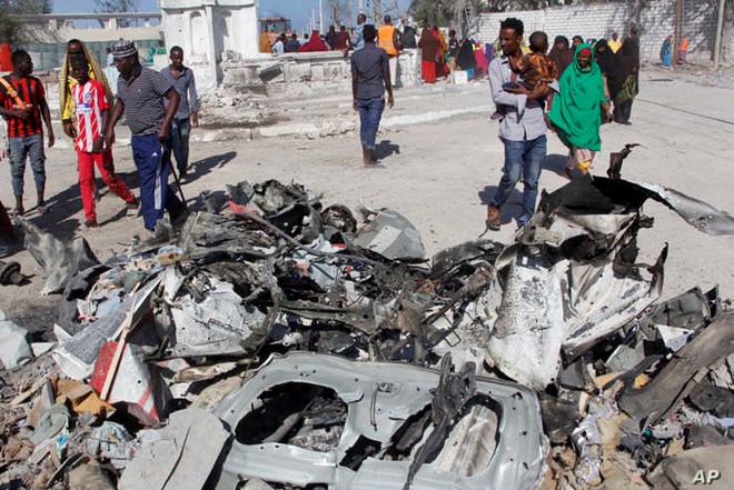 FILE - Somalis walk past debris after a suicide car bomb attack on a government building in the capital Mogadishu, Somalia, Saturday, March 23, 2019. Al-Shabab gunmen stormed the government building after the bomb attack.