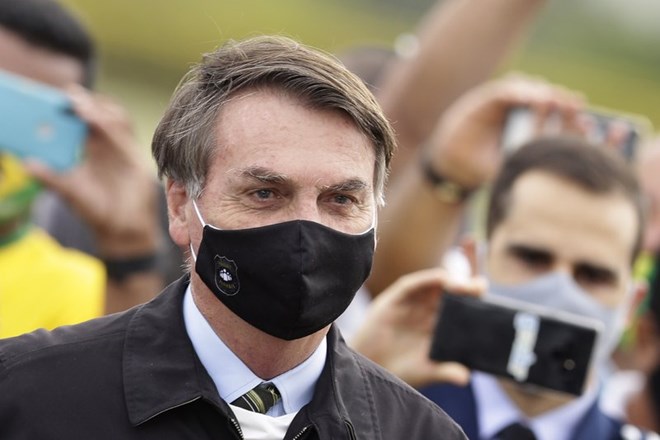 In this May 25, 2020, file photo, Brazil's President Jair Bolsonaro, wearing a face mask amid the coronavirus pandemic, stands among supporters as he leaves his official residence of Alvorada palace in Brasilia, Brazil. Bolsonaro said Tuesday, July 7, he tested positive for COVID-19 after months of downplaying the virus's severity while deaths mounted rapidly inside the country. (AP Photo/Eraldo Peres, File)