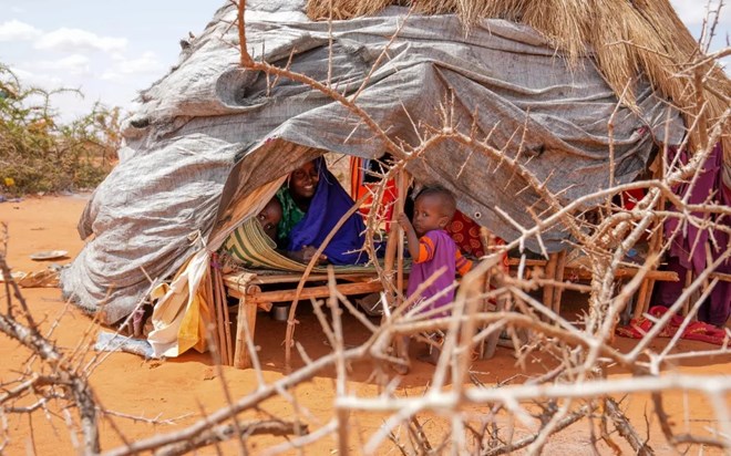 Little Gedi plays with his baby sister and mother inside a makeshift tent at Kaharey IDP camp in Dollow, Somalia. Their house is made of twigs tied together to form a dome. Blankets, tarpaulin and pieces of fabric are fastened to the structure to protect them from the unrelenting heat. Drought and famine forced the family to leave their home in Garbaharrey, they walked for more than 10 days to reach the camp. [Fazel/UNICEF]