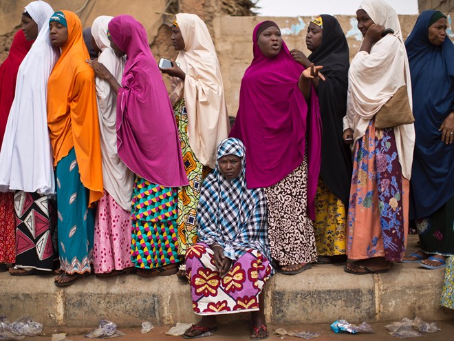 A tired Nigerian woman sits down to rest as others queue, while they face long delays to cast their vote in the afternoon at a polling station in Daura, the home town of opposition candidate Gen. Muhammadu Buhari, in northern Nigeria Saturday, March 28, 2015.