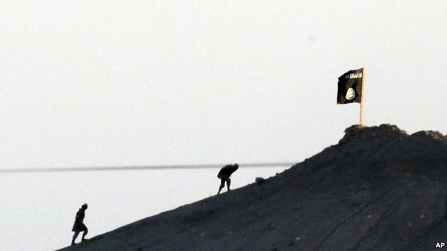 FILE - In this image shot with an extreme telephoto lens and through haze from the outskirts of Suruc at the Turkey-Syria border, militants with the Islamic State group are seen after placing their group's flag on a hilltop.
