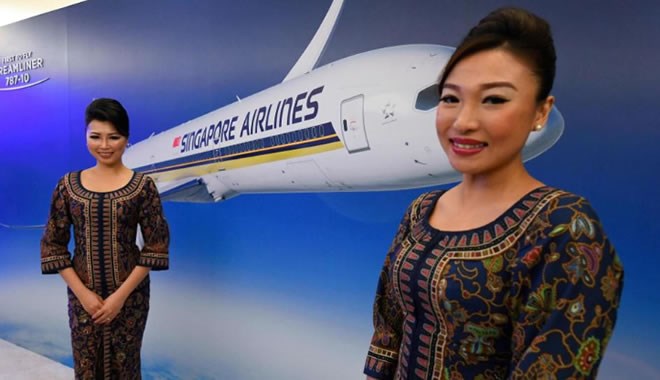 Stewardess stand in front of a poster of Singapore Airlines (SIA) depicting the world's first Boeing 787-10 aircraft prior to its actual arrival at Singapore Changi Airport on March 28, 2018. (Photo credit ROSLAN RAHMAN/AFP/Getty Images)
